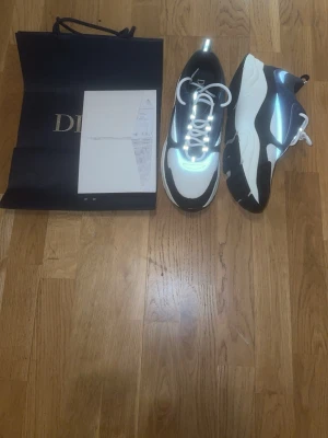 Svarta och vita sneakers - Snygga sneakers i svart och vitt med reflekterande detaljer och vita skosnören. Skorna har en chunky sula och modern design som sticker ut. Perfekta för dig som vill ha något exklusivt och trendigt från ett lyxigt märke. Bara att skriva vid frågor! Priset kan diskuteras😁