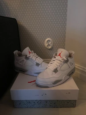 Air Jordan 4 White Oreo sneakers - Säljer ett par Air Jordan 4 White Oreo sneakers. Skorna är vita med grå detaljer och röda inslag på tungan. Klassisk siluett med meshpaneler och läder, samt synlig Air-sula. Perfekta för dig som gillar streetwear och snygga detaljer.