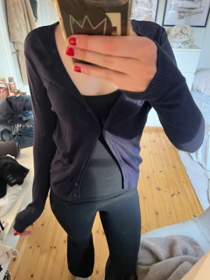 Mörkblå kofta - En stilren mörkblå cardigan med v-ringning och knäppning framtill. Tröjan har långa ärmar och ribbade muddar vid ärmslut och nederkant. Perfekt att slänga över ett linne eller t-shirt för en enkel och snygg look.