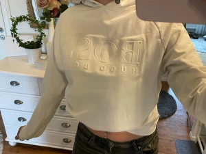 Vit hoodie från Hugo Boss - Säljer en stilren vit hoodie från Hugo Boss med upphöjt logotryck på bröstet. Hoodien har huva och en avslappnad passform som ger en cool och modern vibe. Perfekt för dig som gillar minimalistisk design och vill ha något bekvämt men ändå snyggt. (Går att buda) #hugoboss #vit #hoodie #skjön