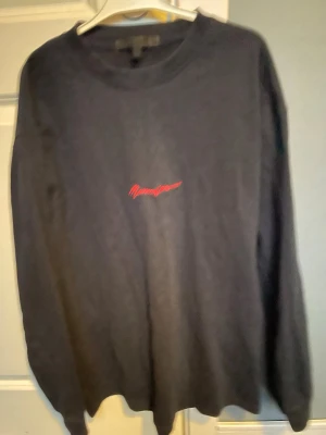 Svart långärmad tröja Manière De Voir - Svart långärmad tröja från Manière De Voir med röd broderad logga på bröstet. Tröjan har en klassisk rund halsringning och är tillverkad i mjukt material som passar perfekt till en avslappnad stil.
