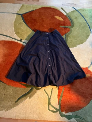 Mörkblå A-linjeformad kjol med knappar - Snygg mörkblå A-linjeformad kjol med knappar framtill. Kjolen har hög midja. Alla knappar är funktionella och kjolen har fickor 