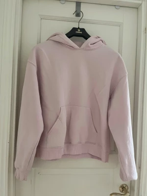 Ljusrosa hoodie med magficka - En basic ljusrosa hoodie med huva och stor magficka framtill. Hoodien har ribbade muddar vid ärmslut och nederkant. Perfekt för en avslappnad och chill stil. Materialet känns mjukt och skönt mot huden. OBS!  Tyvärr är det fläckar på magen och på ena axeln som inte går bort när jag har försökt! Se bilder 