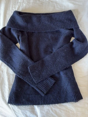Mörkblå off shoulder stickad tröja - Säljer en mörkblå stickad tröja från Gina Tricot med bred off shoulder-krage och långa ärmar. Tröjan har ribbstickade detaljer vid krage, ärmslut och nederkant. Perfekt för dig som gillar en stilren och mysig look.