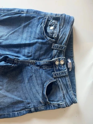 Lowwaist bootcut jeans med dubbla knappar - Snygga blå bootcut jeans med dubbla knappar i midjan och klassiska fem fickor. Jeansen har ljus tvätt och tydliga sömmar, vilket ger en avslappnad vibe. Perfekta att matcha med allt.