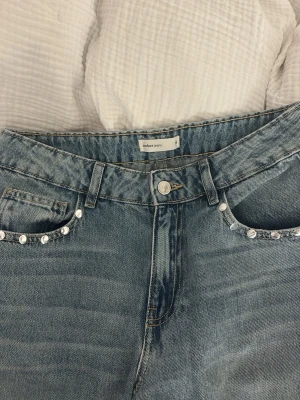 Ljusblå jeans med pärldetaljer - Snygga ljusblå jeans från gina tricot med raka ben och pärldetaljer längs fickorna fram och bak. Klassisk femficksmodell med bälteshällor och knappgylf. Tillverkade i denim med en cool tvättad look. Använd ungefär 1 gång så nästan i nyskick! 