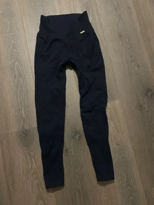 Mörkblåa seamless sportleggings - Snygga mörkblåa seamless leggings med hög midja och ribbade detaljer längs benen. Tillverkade i stretchigt funktionsmaterial som passar perfekt för träning eller chill. Diskret logga framtill vid midjan. Tight passform och långa ben.