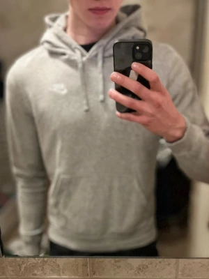 Grå hoodie från Nike med huva - Säljer en stilren grå hoodie från Nike med klassisk vit liten logga på bröstet. Tröjan har huva med snörning. Passar till alla tillfällen, och lätt att bara slänga på sig. Pris inte hugget i sten.