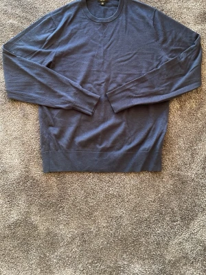 Mörkblå merinoull tröja - En stilren mörkblå stickad tröja med rund hals och långa ärmar. Tröjan har ribbade muddar vid ärmslut och nederkant. Materialet känns mjukt och lätt, perfekt för lager på lager. Passar dig som gillar en enkel och klassisk look.