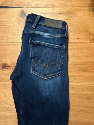 Mörkblå Replay jeans med slitningar - Snygga mörkblå jeans från Replay med klassisk femficksdesign och diskreta slitningar framtill. Jeansen har raka ben och detaljerade sömmar vid fickorna. Perfekta för en trendig och avslappnad look.