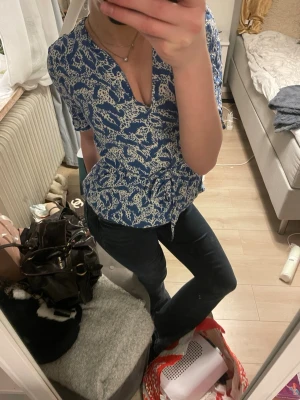 Blå omlottblus med vitt mönster - Snygg blå omlottblus/kort klänning med vitt mönster och knyt i midjan. Blusen har v-ringning och korta ärmar. Kommer från Vila i storlek 36. 