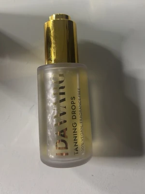 IDAWARG Tanning Drops - Säljer IDAWARG Tanning Drops i en frostad glasflaska med guldfärgad pump. Produkten är 100% vegansk och doftfri, perfekt för dig som vill ha en naturlig solkysst look. Enkel att blanda i din vanliga hudvård för gradvis brun utan sol.