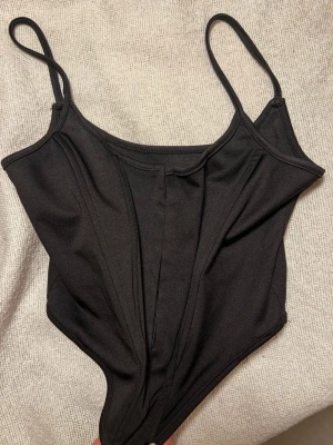 Korsett svart - Svart korsett med smala axelband och en figurnära passform. Den har en korsettliknande design framtill. Passar S-M