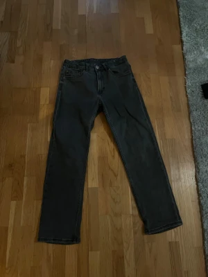 Svarta raka jeans - Säljer ett par svarta jeans med rak passform och klassisk femficksdesign. Jeansen har knapp- och dragkedjegylf samt diskreta sömmar. Perfekta för en stilren och enkel look.