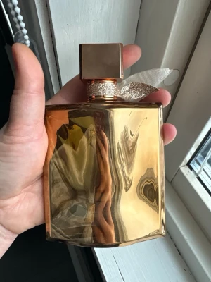 La Vie Est Belle - , i en glänsande guldig färg med elegant banddetalj runt halsen. Flaskan har en fyrkantig form och ett matchande guldigt lock som ger en exklusiv känsla. 