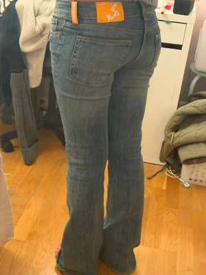 Blå bootcut jeans från weekday - Säljer ett par klassiska blå bootcut jeans från weekday  med orange patch och detaljer. Jeansen har fem fickor, låg midja och utsvängda ben. Perfekta för dig som gillar en retro vibe och vill ha ett par snygga jeans med skön passform. knappt använda.