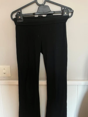 Svarta ribbade mjukisbyxor - Svarta mjukisbyxor med ribbad struktur och utsvängda ben. Byxorna har hög midja och är tillverkade i ett mjukt och stretchigt material som ger en skön passform. Perfekta för en avslappnad och trendig look.