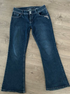 Mörkblå bootcut jeans med låg midja - Snygga mörkblå bootcut jeans med låg midja och klassiska fickor fram och bak. Jeansen har dubbla knappar i midjan och diskreta slitningar för en cool look. Perfekta för dig som gillar en avslappnad men trendig stil. Om du har några frågor är det bara att skicka☺️☺️