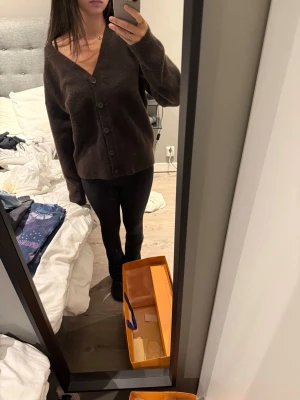 Mörkbrun oversized kofta - Mysig mörkbrun kofta med v-ringning och stora knappar framtill. Oversized passform och långa ärmar, perfekt att slänga på sig över en t-shirt eller linne. Enkel och stilren design som passar till det mesta.