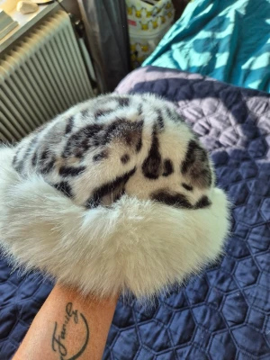 Leopardmönstrad pälsmössa - Snygg pälsmössa med leopardmönster i svart, grått och vitt. Mössan har en bred, fluffig kant i ljus fuskpäls som ger en lyxig känsla. Perfekt accessoar för att sticka ut och hålla värmen under kalla dagar.