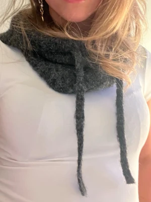 Mörkgrå stickad halsduk med snören - Mysig mörkgrå balaclava  i stickat material med två långa snören framtill.