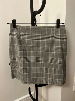 Grå rutig kortkjol från Lindex - Snygg grå kortkjol från Lindex med klassiskt rutigt mönster. Kjolen har en rak passform och är tillverkad i ett mjukt material som känns bekvämt. Perfekt att matcha med en enkel topp eller stickad tröja för en trendig look.