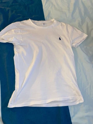 Vit t-shirt från Ralph Lauren - Klassisk vit t-shirt från Ralph Lauren med den ikoniska lilla blå loggan broderad på bröstet. T-shirten har rund halsringning och korta ärmar. Perfekt basic-plagg som funkar till allt och är tillverkad i mjuk bomull för skön känsla.