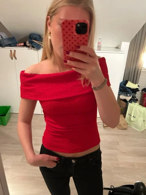 Röd offshoulder topp från H&M - Trendig röd offshoulder topp från H&M i stretchigt, ribbat material. Toppen sitter tight, perfekt för att skapa en snygg siluett. Enkel men ändå iögonfallande design som lyfter vilken outfit som helst. Prislapp kvar!
