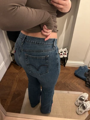 Blå bootcut jeans från Levi's - Säljer ett par klassiska blå bootcut jeans från Levi's med femficksdesign och tydliga sömmar på bakfickorna. Jeansen har normal midja och är tillverkade i denim med lätt stretch för skön passform. Motsvarar en storlek M