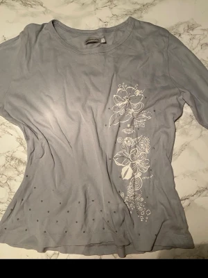 Ljusblå blommig tröja med tryck - Snygg vintage ljusblå tröja från ANALAGA med vita blommiga tryck och små prickar på framsidan. Klassisk rund halsringning. Perfekt för dig som gillar en enkel men ändå unik stil. Tillverkad i mjuk bomull för skön känsla.