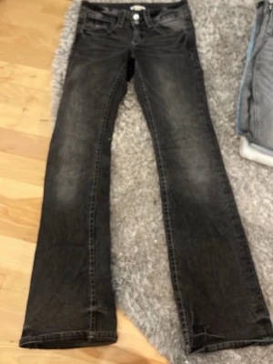 Grå bootcut jeans - Säljer ett par mörk grå bootcut jeans med slitningar och klassisk femficksmodell. Jeansen har låg midja och boutcut ben, perfekta för en avslappnad och trendig look. Materialet är denim med lätt stretch för extra komfort. 