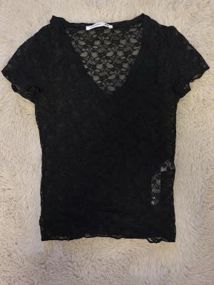 Svart spetsblus från Terranova - Säljer en svart,  spetsblus från Terranova i storlek XS. Blusen har v-ringning, korta ärmar och ett blommigt spetsmönster som ger en elegant och trendig look. Perfekt att styla lager på lager eller med ett linne under.