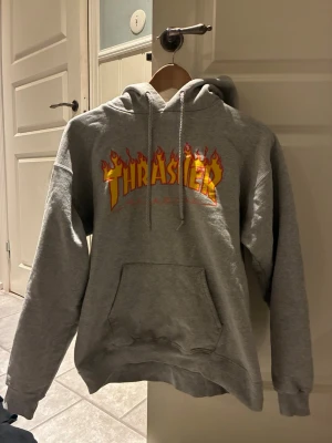 Grå Thrasher hoodie med flames - Säljer en grå hoodie från Thrasher  flames-loggan i gult och rött, inga större tecken på använding 💞