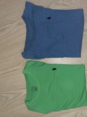Blå och grön t-shirt från Polo Ralph Lauren - Två stilrena t-shirts från Polo Ralph Lauren, en i blått och en i grönt. Båda har klassisk passform, rund halsringning och den ikoniska broderade loggan på bröstet. Perfekta för en avslappnad och snygg look.  En för 90 två för 150