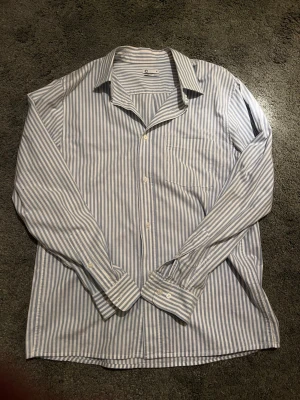 Blåvit randig skjorta från Cubus - Snygg blåvit randig skjorta från Cubus i relaxed fit. Skjortan har klassisk krage, lång ärm och knäppning framtill. Perfekt för en chill och stilren look. Tillverkad i mjuk bomull som känns skön mot huden.