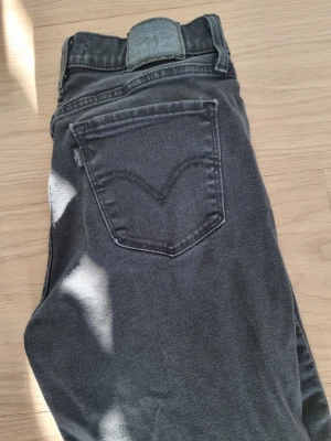 Svarta Levi's jeans - Säljer ett par svarta jeans från levis. Jeansen har en diskret tvättad look och Levi's ikoniska bakficka med V-söm. Perfekta till en avslappnad stil och funkar året runt. Ungefär storlek S