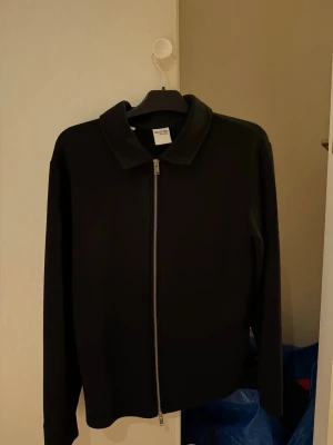 Svart jacka från Selected med dragkedja - Stilren svart jacka från Weekday med hel dragkedja framtill och klassisk krage. Jackan har lång ärm och en clean, minimalistisk look som passar till det mesta. Perfekt för dig som gillar enkel och modern stil.