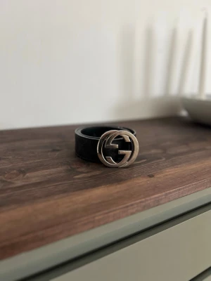 Svart Gucci bälte med silverdetalj - Snyggt svart bälte från Gucci med klassiskt GG-spänne i silver. Bältet har diskret mönster längs hela remmen och är tillverkat i skinn. Perfekt accessoar för att lyfta vilken outfit som helst. Självklart äkta!