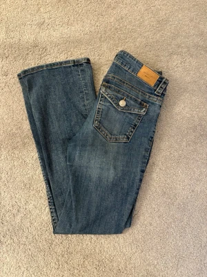 Blåa bootcut jeans med knappficka - Supersnygga blå bootcut jeans, lågmidjade med knappfickor baktill och stretchigt tyg.