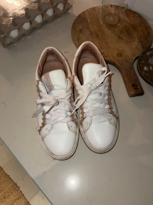 Vita sneakers från See By Chloé - Snygga vita sneakers från See By Chloé med beige detaljer och vågiga kanter. Skorna har klassisk låg modell, vita snören och logga i guld på hälen. Tillverkade i läder med mjuk innersula för extra komfort.