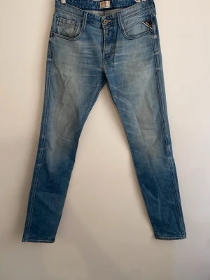 Replay jeans  - Snygga blå jeans från Replay med raka ben och klassisk femficksmodell. Jeansen har en ljus tvätt med slitningar och kontrastsömmar. Tillverkade i bomull med dragkedjegylf och detaljerade bakfickor. Perfekta för en avslappnad och trendig look.