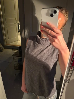 Grå ärmlös polotopp - Säljer en grå ärmlös polotopp med hög krage. Toppen har en loose passform och är stickad, vilket gör den både snygg och bekväm. Perfekt att styla med jeans eller kjol för en trendig look.