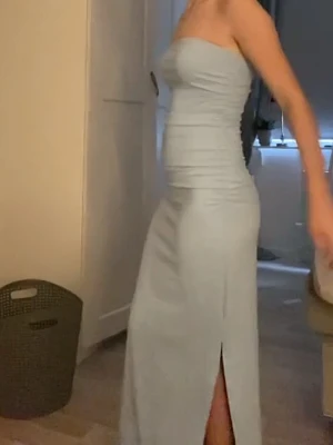 Ljusblå långklänning med slits - Elegant ljusblå långklänning med figurnära passform och slits framtill. Klänningen är axelbandslös och har en stilren, enkel design som framhäver siluetten. Perfekt för dig som vill ha en klassisk och modern look.