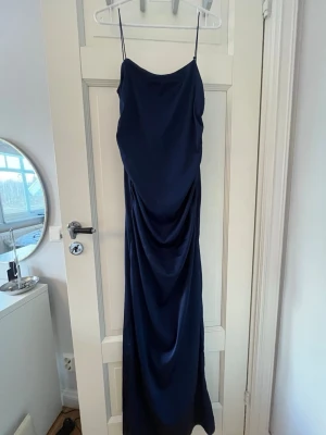Mörkblå balklänning  - Elegant mörkblå långklänning med tunna axelband med öppen rygg. Klänningen är tillverkad i satin. Perfekt för dig som vill ha en stilren och trendig look. Perfekt till balen. Använd en gång på Supén. Nypris 899