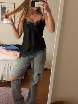 Vitalt Zara Linne  - Snygg svart linnetopp med tunna axelband och spetsdetaljer längs urringning och nederkant. Toppen har en feminin v-ringning och är perfekt för att skapa en trendig look. Materialet känns mjukt och följsamt mot huden.