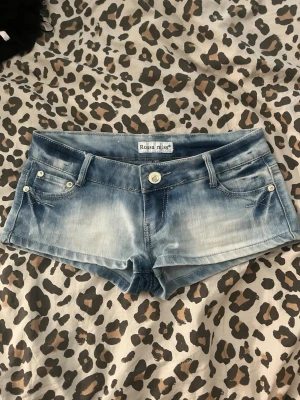 Blå denimshorts från Rossa Miss - Snygga blå denimshorts från Rossa Miss med låg midja och klassisk femficksdesign. Shortsen har slitna detaljer och ljus tvätt för en avslappnad look. Perfekta för varma sommardagar och enkla att matcha med olika toppar.