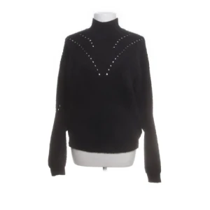 Svart polotröja med detaljer - Snygg svart polotröja med dekorativa detaljer framtill. Tröjan har långa ärmar och en klassisk polokrage, perfekt för kyligare dagar. Den är en mohairmix så man blir extra varm! 