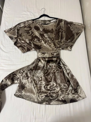 Brun beige silkes klänning  - Snygg klänning med silkes material. Vida ärmar och tillhörande midjebälte. Perfekt för chill hemma eller när du vill känna dig extra bekväm. Har knappt använda men väldigt snygg på från Zara storlek M. 