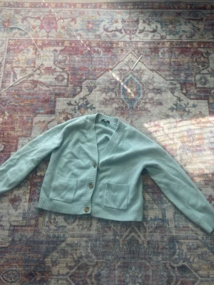 Ljusblå kofta från Uniqlo - Mysig ljusblå kofta från Uniqlo med v-ringning och tre knappar framtill. Koftan har två praktiska fickor och ribbade muddar vid ärmslut och nederkant. Perfekt för lager på lager och enkel att matcha med olika outfits.