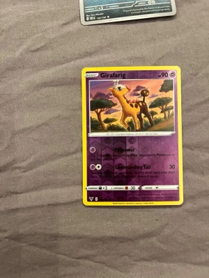 Pokémonkort Girafarig - Säljer ett Pokémonkort med Girafarig-motivet. Kortet har lila och gul ram, klassisk Pokémon-design och är tryckt på glansigt pappmaterial. Perfekt för samlare eller dig som gillar att spela Pokémon TCG.
